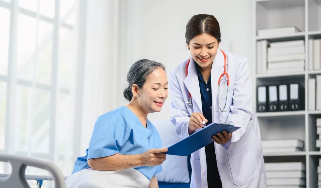 woman in a blue hospital gown is sitting in a hospital bed with a doctor standing next to her